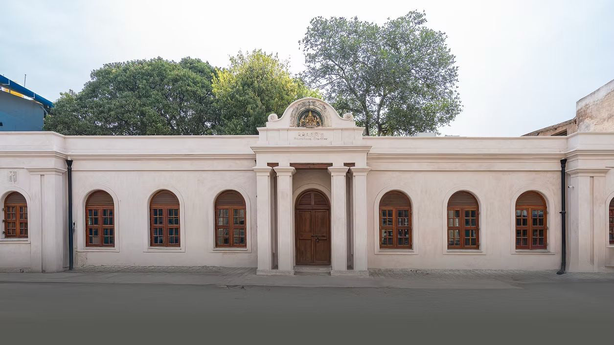 White building with arched windows and a central door, surrounded by trees.