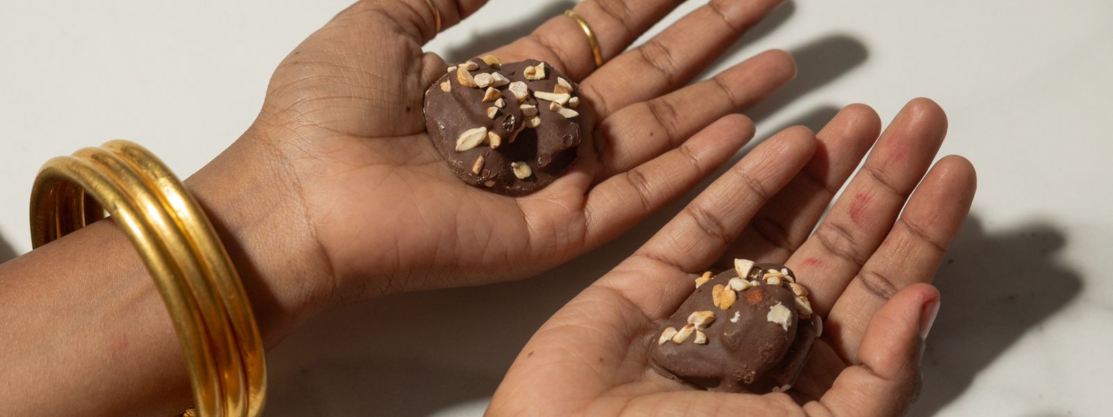 Two hands holding chocolate pecan rocks with sprinkled nuts on a light background
