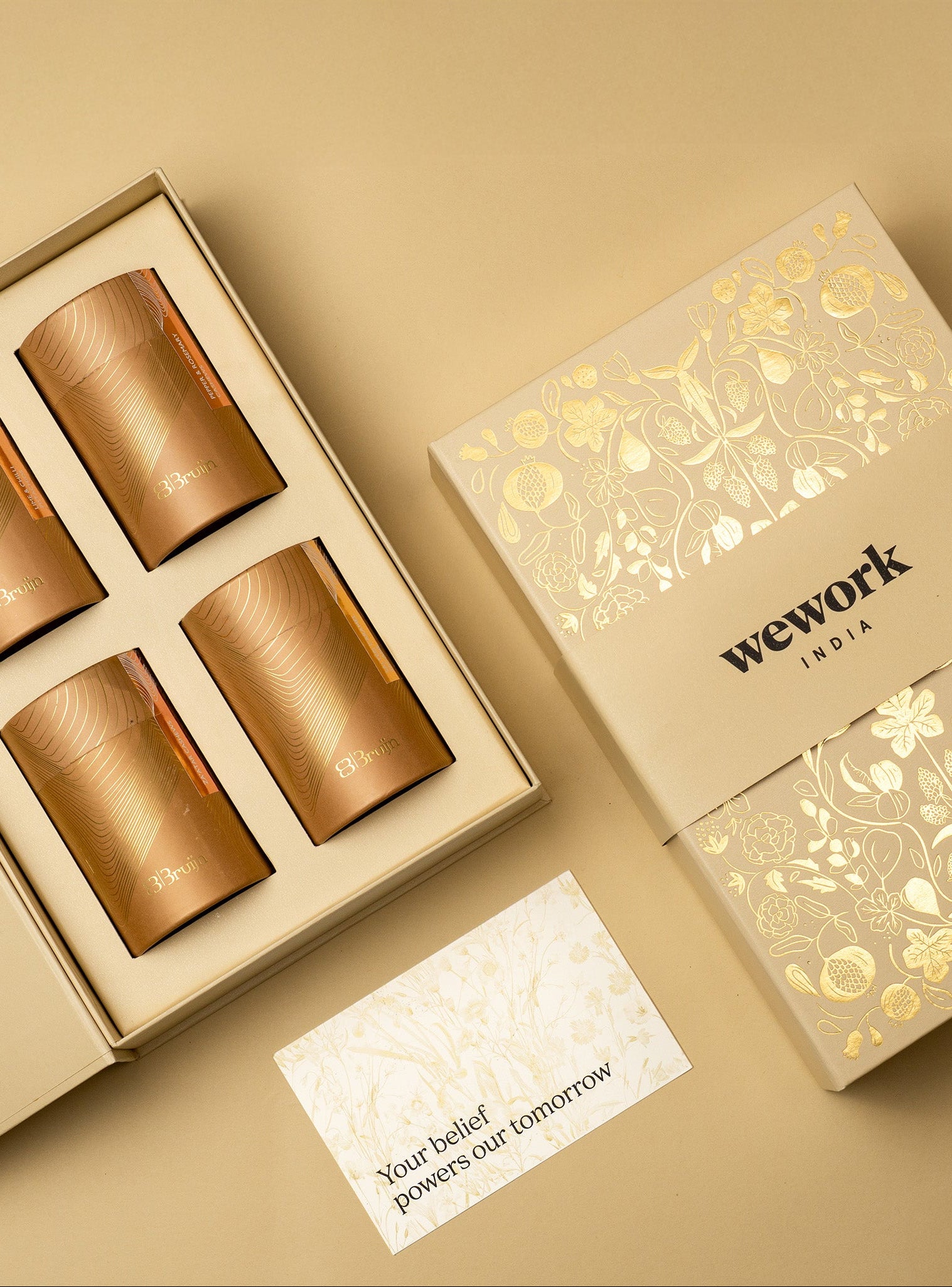 Set of gold cylindrical containers containing savoury nuts in a decorative box with 'wework' branding on a beige background.
