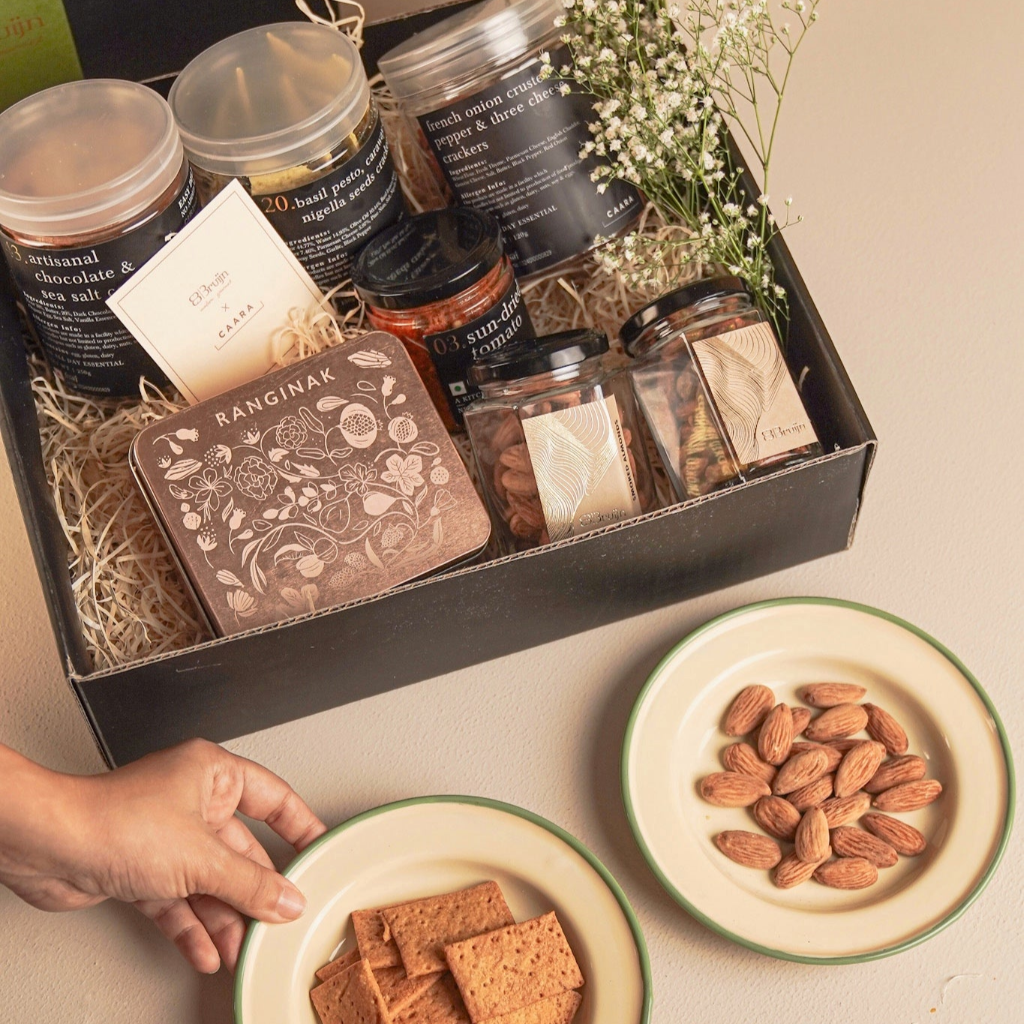 Spice set in a gift box with a plate of crackers and almonds on a neutral background