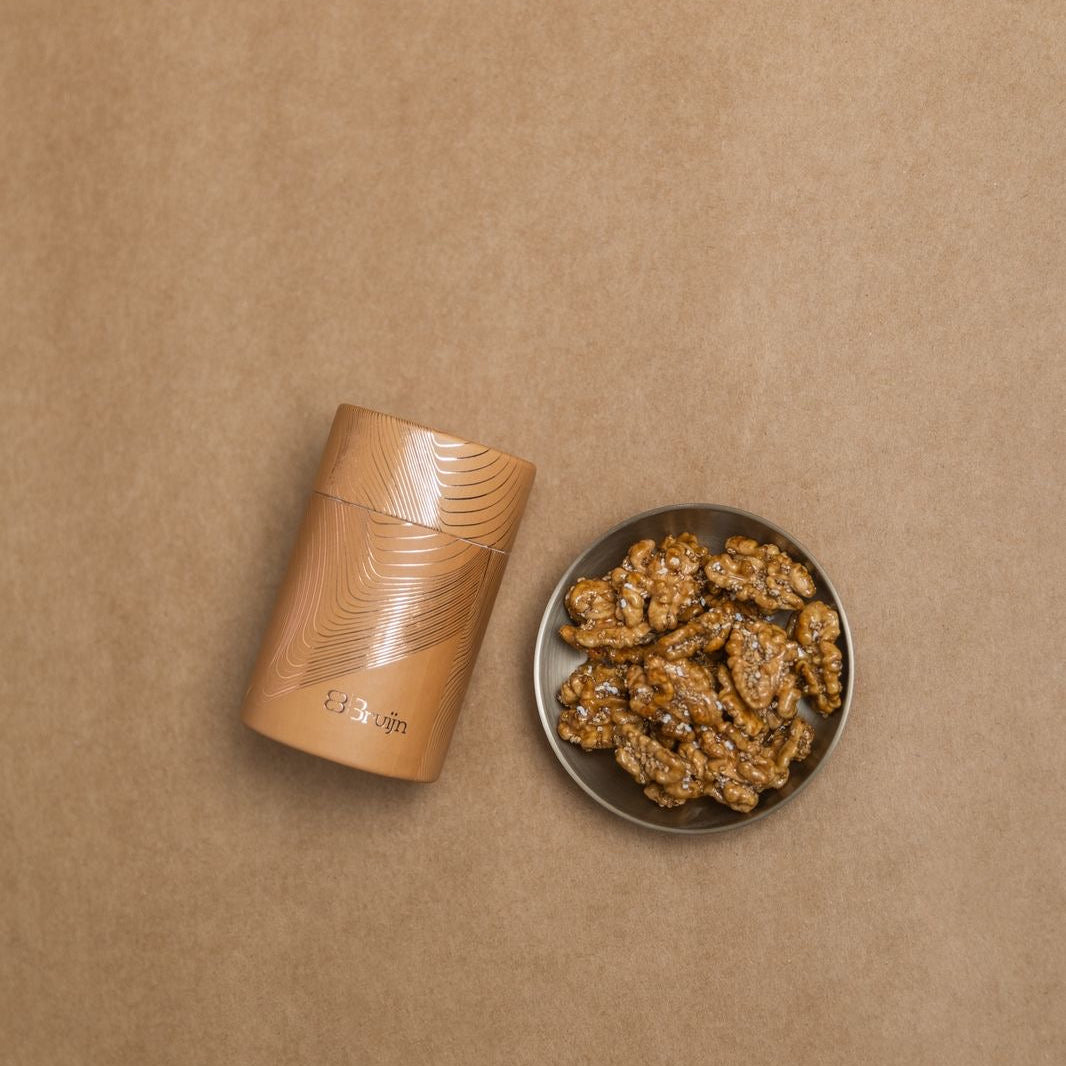 Brown cylindrical container with roasted walnuts caramelized with date sap jaggery and sprinkled with white sesame