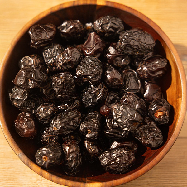 Wooden bowl filled with Ajwa dates on a wooden surface