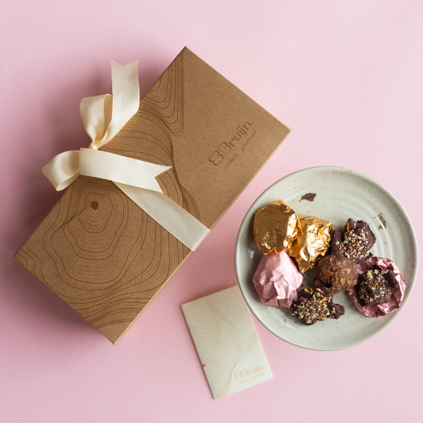 Gift box with a bow, a plate of chocolate truffles, and a card on a pink background