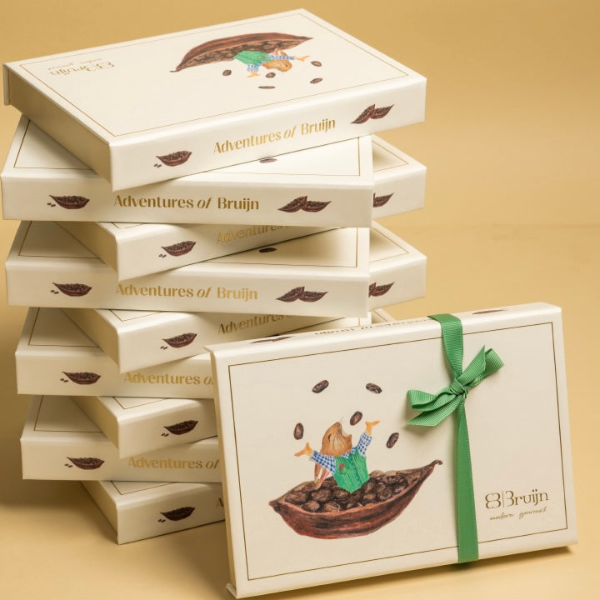 Stack of 'Adventures of Bruijn' branded boxes with a decorative box featuring a green ribbon on a beige background.
