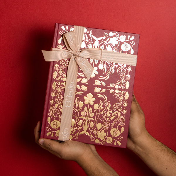 Red gift box with gold floral patterns and a beige ribbon held against a red background