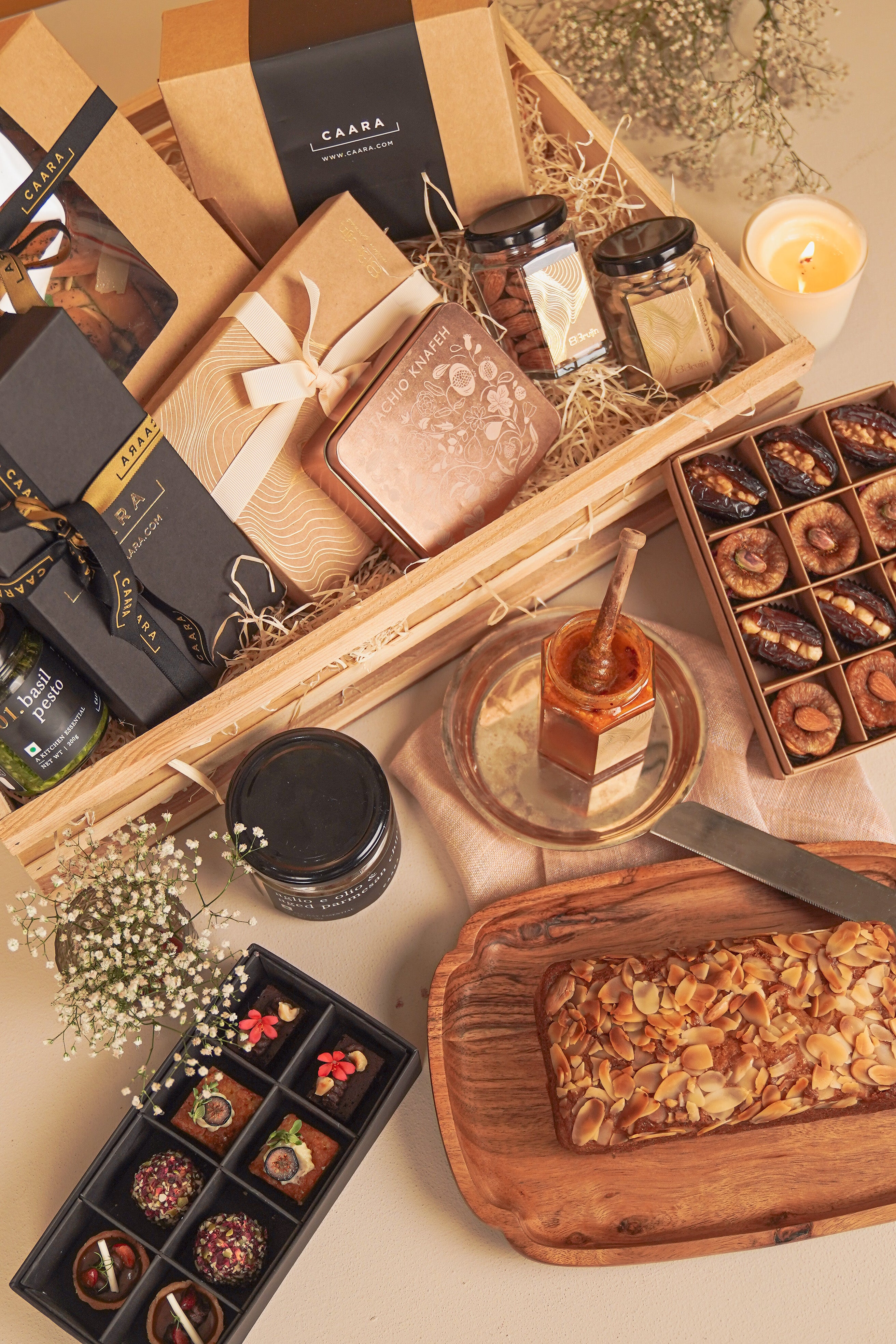 Gourmet gift basket with chocolates, candles, and a loaf of bread on a wooden surface.