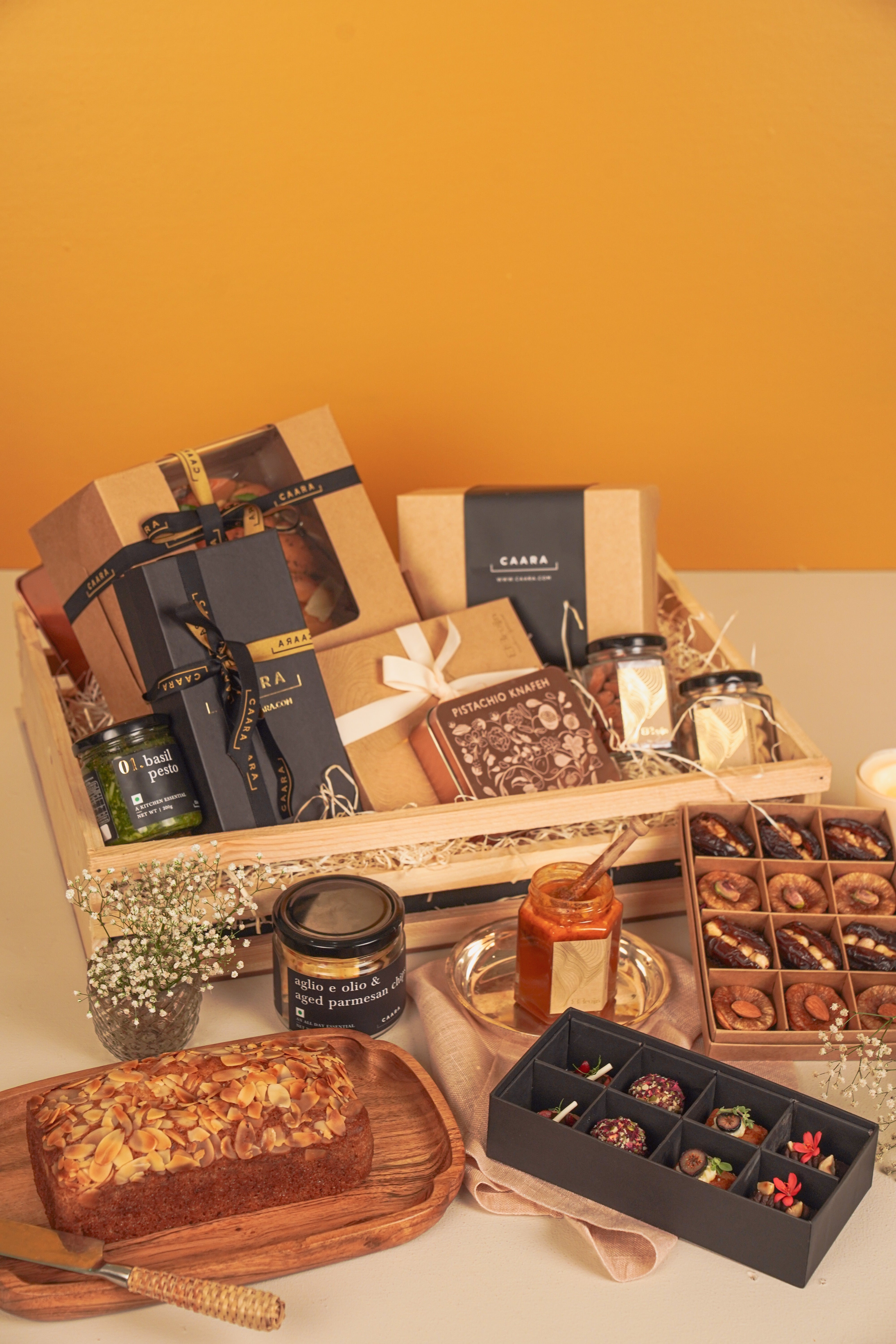 Gourmet gift basket with various items including a loaf of bread, chocolates, and jars on a wooden table.