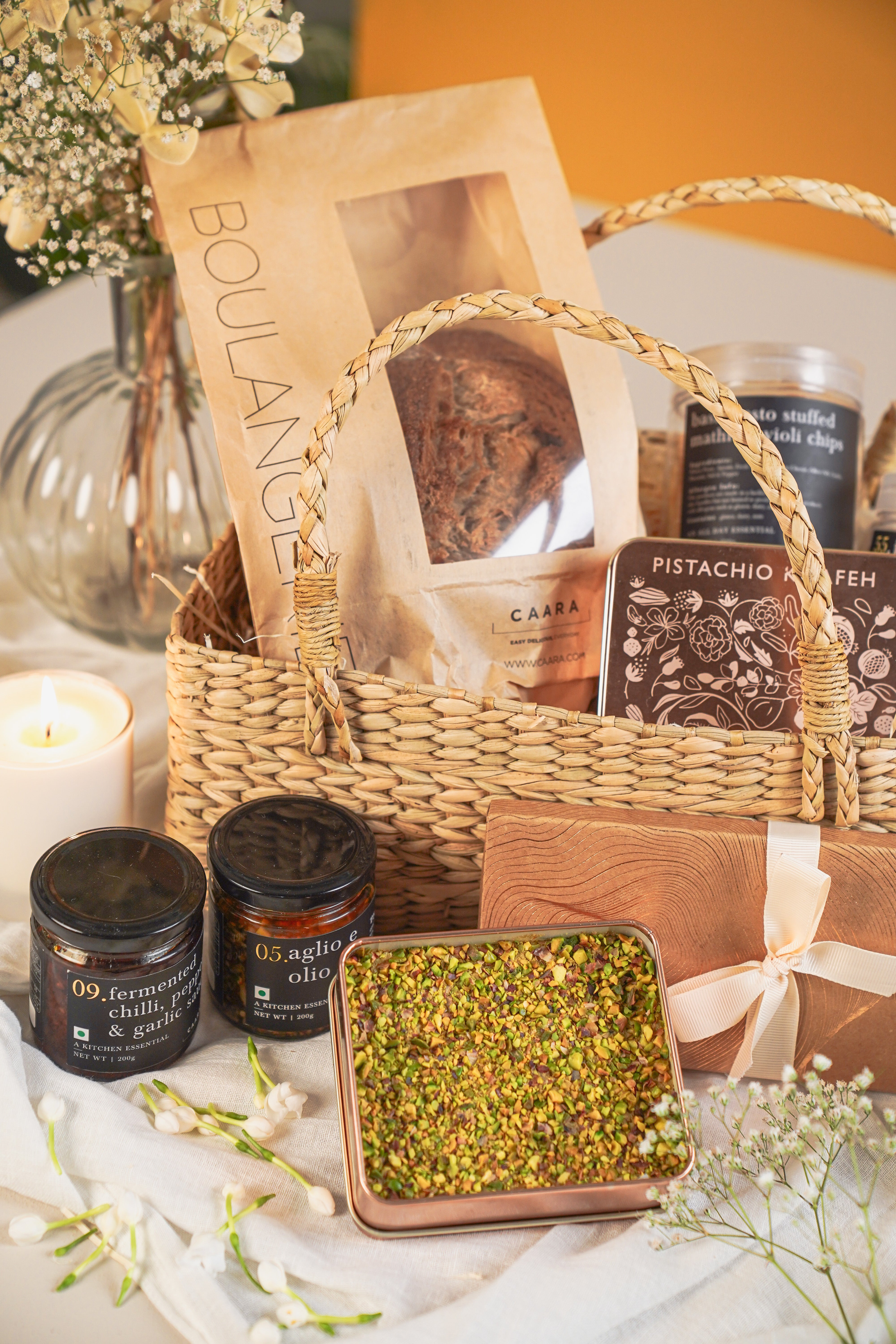 Gift basket with various items including a candle, a box of tea, and a container of pistachios on a decorative surface.