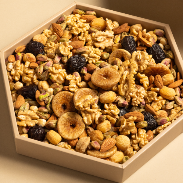 An assortment of dried fruits and nuts including pistachios, hazelnuts, walnuts, almonds, figs, apricots, dates, and raisins, presented hexagonal tray.