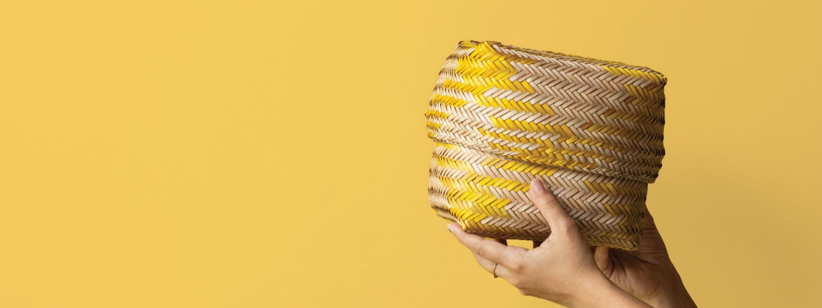 Hand holding a woven basket with yellow and brown pattern against a yellow background