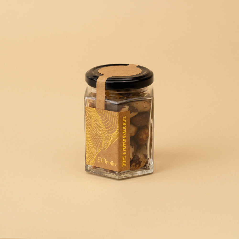A clear glass jar filled with Brazil nuts, featuring a black lid and a gold label with the brand name Bruijn. The product is photographed on a solid beige background.