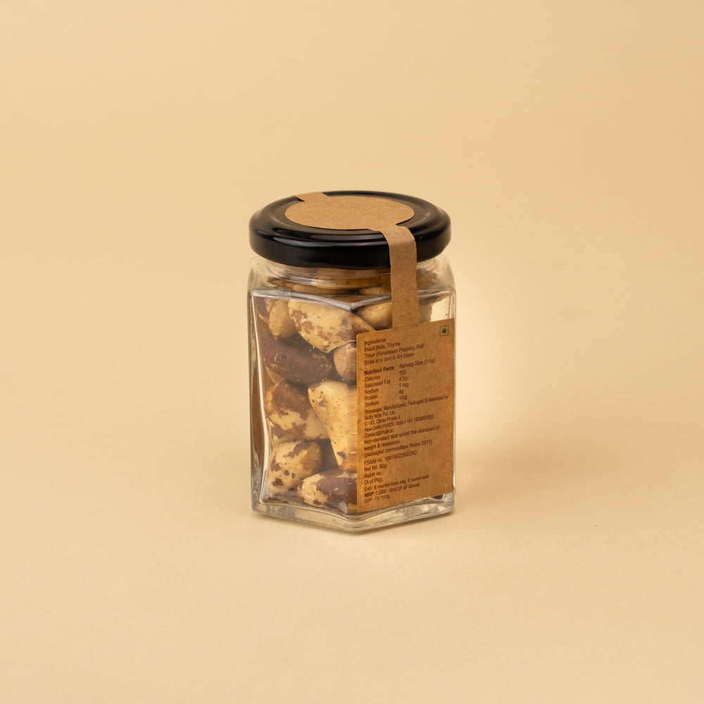 A clear glass jar filled with Brazil nuts, featuring a black lid and a gold label with the brand name Bruijn. The product is photographed on a solid beige background.