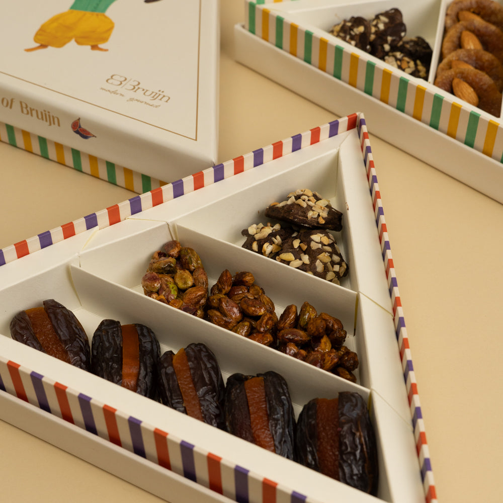 A triangle box that contains stuffed dates, honey and nut clusters, chocolate rocks 