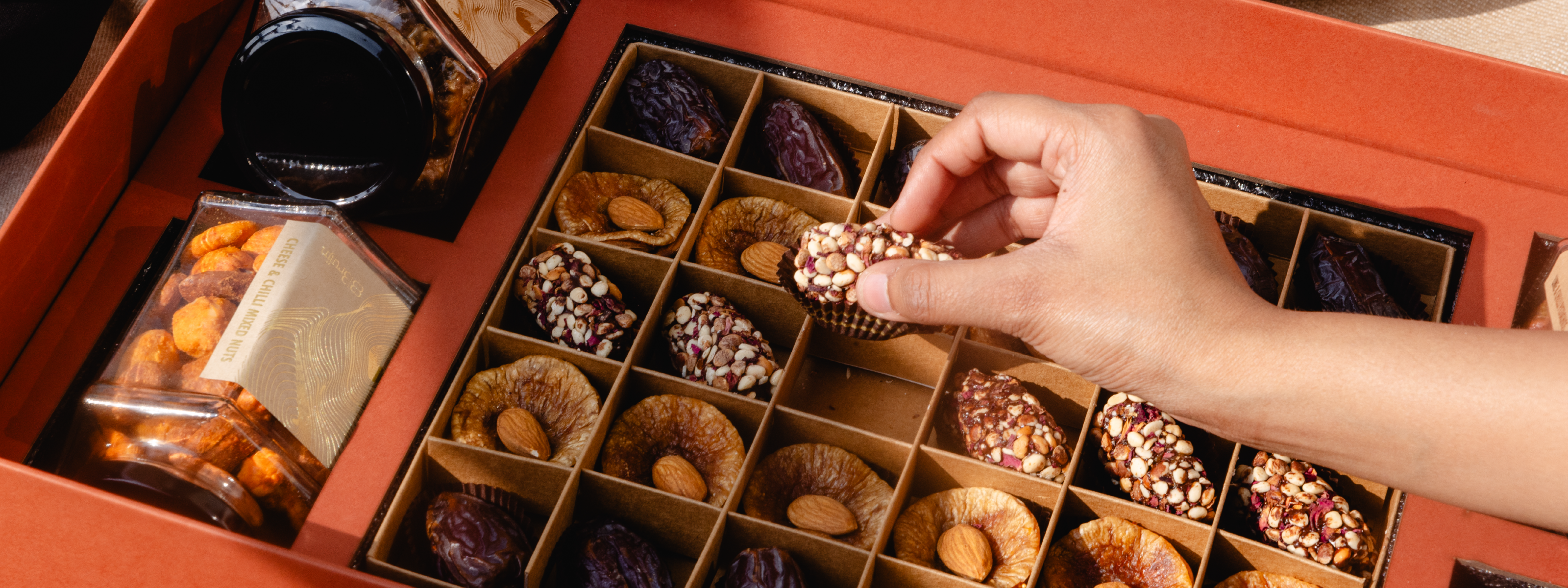 Hand picking a nut from a date of assorted nuts and dried fruits.